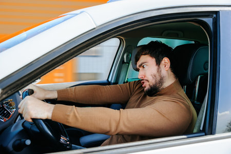young bearded man at the wheel of a car with bizarre eccentric emotions. males with facially obvious emotions different funny, ridiculous idioticの写真素材
