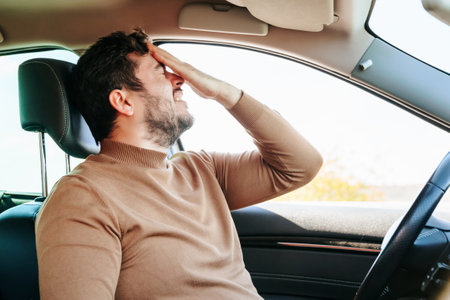 A terrible grimace of pain on the face of a young male driver, a hand on his forehead, a grimace on his face. Headache often haunts drivers. Hard work. Emotions and people.の写真素材