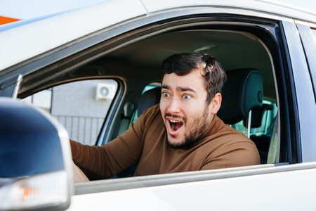 A frightened surprised young guy in a car behind the wheel screams with bulging eyes and looks ahead. The man cringed and shows emotions with great feeling. Man, human feelings.の写真素材