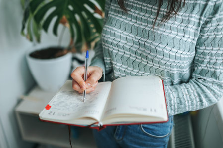 Unrecognizable girl woman standing makes important notes in workbook, pen on paper. Urgently need to...
