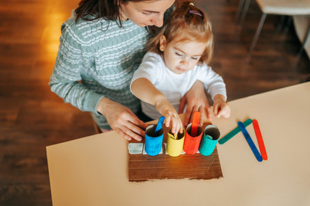 Focused little girl playing a young mother doing experiments with rainbow colors in a modern kitchen together. Happy mother brings up her little daughter at home, developing her cognitive processes.の写真素材