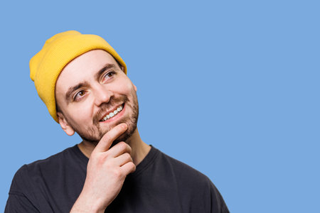 Thinking guy looking up and around on blue background. Pensive confused guy leaning hand, rubbing beard while thinking over difficult choice, People sincere emotions, lifestyle concept.の写真素材