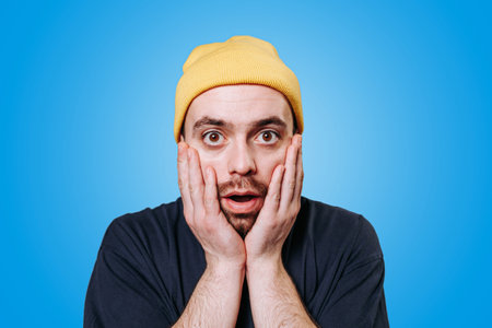 Shocked stunned People sincere emotions, on blue background, studio shot. Bearded man feeling amazed astonished and looking big eyes surprised at camera, gogglesの写真素材