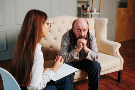 a bald senior man looking at a young nurse. Mature female psychiatrist communicating with sad 60s patients, senior worried, serious elderly, worried mature, stress, lonely, therapist, patient,の写真素材