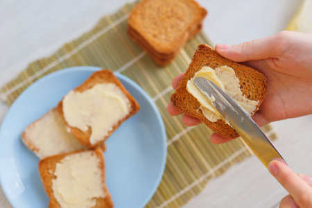 process of preparing a healthy breakfast is captured in a close-up shot of hands spreading butter on bread. Starting the day off right with a healthy breakfast of toasted bread spread with butterの写真素材