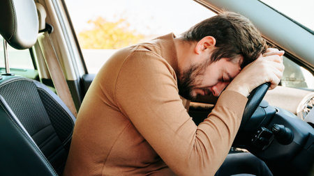 Tired young car driver sleeps in his car with his head on the steering wheel. The young driver falls asleep on the steering wheel. Working overtime.の写真素材
