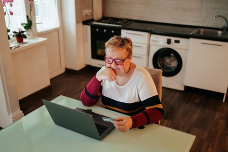 A woman, who is old and overweight, is depicted making an e-commerce purchase from home using her laptop and credit card, looking glad and authentic.の写真素材