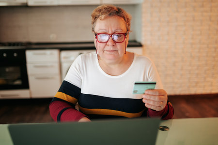 A fat woman, wearing eyeglasses, is using her laptop and credit card to browse and purchase items from e-commerce websites. She is comfortably seated at home, enjoying the convenience and comfortの写真素材
