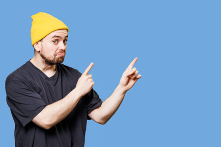 portrait of a handsome and stylish bearded guy in studio shot, grimacing with a bizarre expression while pointing to free space, looking at the camera and providing ample copy space.の写真素材
