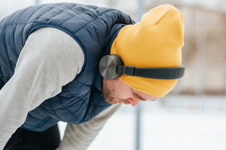 A male with headphones he looks tired, he leans down athlete braves the winter weather to stay on track with his exercise routine. With headphones in and a look of intense focus,の写真素材