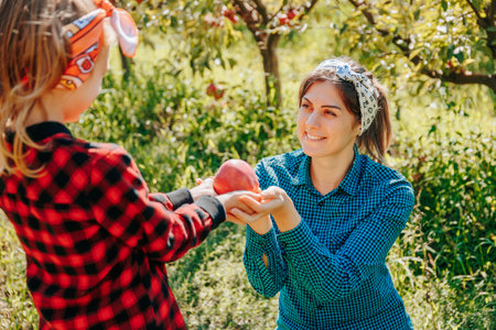 A proud mother and her daughter sharing a special moment while picking apples together in their familys orchard.の写真素材