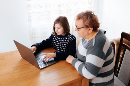 old women of all ages studying together at home, using their laptops to research and learn. The kid is explaining a new idea to her peers, who listen attentively, eager to expand their knowledgeの写真素材