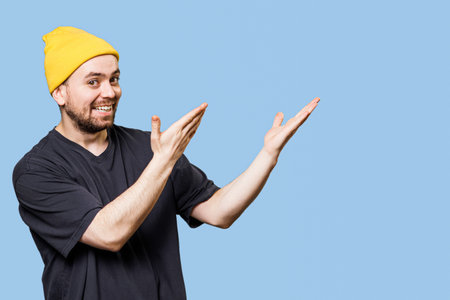Studio shot with copy space captures an expressive and gesture man, pointing to free space, looking at the camera with a joyous expression and satisfied smileの写真素材