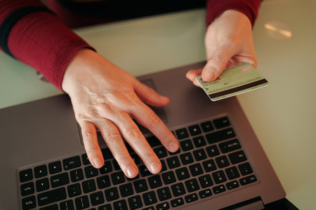 Womens hands on a laptop, using a credit card to make an online purchase. The photo captures the ease and confidence of shopping online, with a clear focus on the hands and credit card.の写真素材