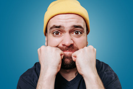 close up portrait of a violent bearded young male, his expression one of anger as he looks directly at the camera. studio shot on the blue background,の写真素材
