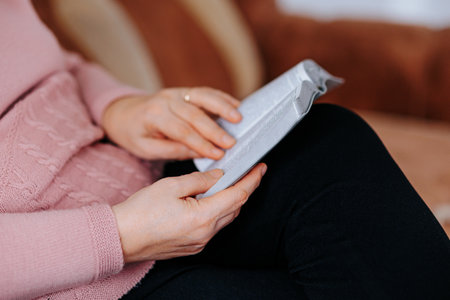 Senior Hands Close-Up Holding a Book for Learning and Enjoyment at Home, Intense Reading Close-Up of Unrecognizable Hands Holding Literatureの写真素材