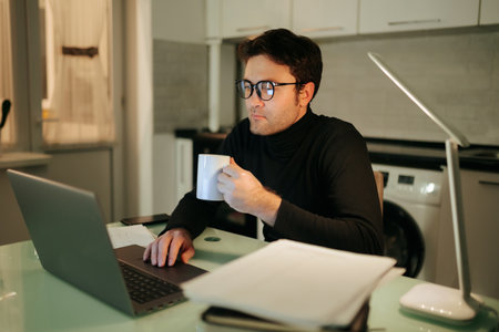 The Night Owl Young Adult Working Late from Home, A young man is using his laptop and working late into the night, as he tackles his freelance job from the comfort of his own home.の写真素材