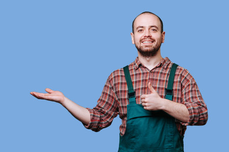 The expressive smiling guy gives a thumbs up with outstretched hand, exuding joy and contentment in the blue background studio shot. copy space, Man spreading his arms with a joyful expressionの写真素材