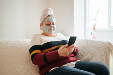 Real People and Real Skincare A photo of a pretty, old woman enjoying her skincare routine in her living room with a mask on her face and music playing in the background. authenticity and realityの写真素材