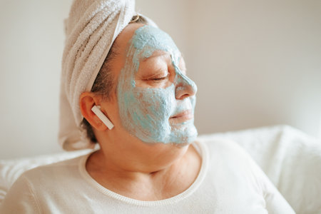 At-Home Beauty for Older Women An overweight senior woman indulges in a relaxing skincare routine at home, complete with headphones to listen to music, a facial mask, and the comfortの写真素材