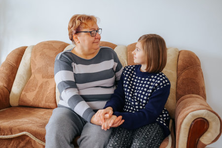 A candid snapshot of a grandmother and her granddaughter sitting on the sofa, reading a book together and deepening their bond.の写真素材