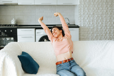 Beautiful Brunette is Waking up in the Morning, Stretches in the sofa. stretching arms up and left to get more energy and strength, smiling happilyの写真素材