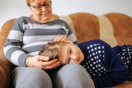 A heartwarming family portrait of a grandmother and her granddaughter sitting on the sofa hands on head, surrounded by other family members and smiling with joy and contentment.の写真素材