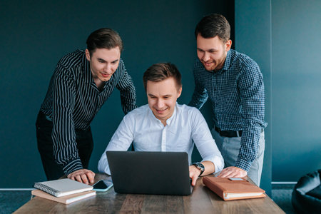 A manager and his two co-workers, all young adults, intently focused on their laptops as they work on a deadline. Three young colleagues, all men, collaborating in a bright, each with a laptopの写真素材