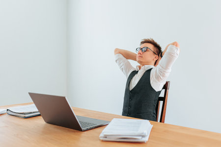 An office worker leans back in his chair, enjoying a moment of relaxation with his eyes closed and a satisfied expression on his face, as the sunlight streams into his indoor workspace.の写真素材