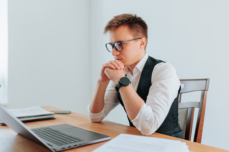 middle-aged office worker in a traditional business suit, sitting at a large, elegant desk in a stately office. Hes wearing glasses and appears to be deep in thought as he works on his laptop,の写真素材