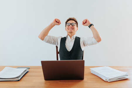 A businessman stands alone at home office, hands raised in victory after closing a major deal. The satisfaction and happiness he feels is evident as he revels in his achievement.の写真素材