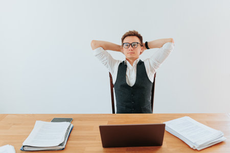 A man dressed in professional attire sits at his desk with a satisfied smile on his face, having completed a successful project on his laptop in the office.の写真素材