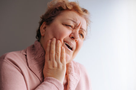 At-Home Despair Sad Senior Woman Coping with Tooth Pain. An aged woman suffers from a toothache, showing signs of stress and discomfort.の写真素材