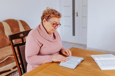 An older woman, glasses on her face, sits in her home with a book in hand, the weight of the world lifting off her shoulders as she becomes lost in the story. Her glasses provide the perfect lensの写真素材