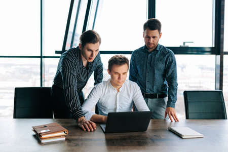 Three young men hard at work in their office, typing away on their laptops. Colleagues collaborating on a new business idea, all with their laptops at the ready.の写真素材