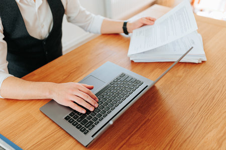 A close-up of a males hands typing on a laptop keyboard from a top view angle, with his office desk and technology in the background.の写真素材