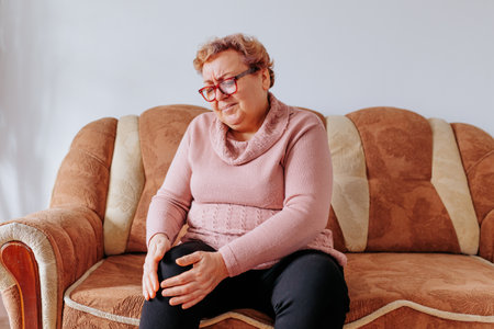 Aging Gracefully Managing Leg Pain at Home for Senior Women, An aged woman trying to relieve her leg pain with a heat pack, feeling the weight and stress of being overweight at home.の写真素材