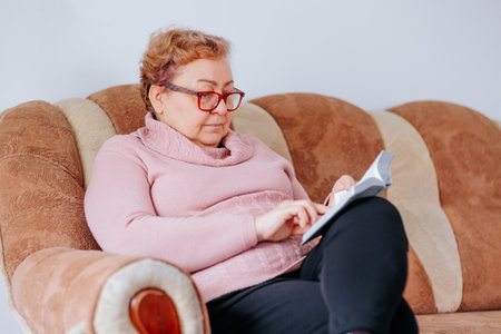 Reading is a passion that never fades, as evidenced by this senior woman who is fully engrossed in her book. Her glasses perched on her nose and a slight smile on her face show just how muchの写真素材