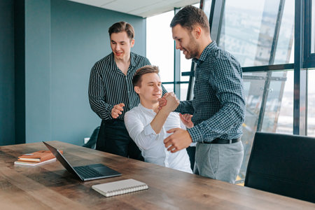 Successful teamwork of three men using laptops at work in the office. Delighted male coworkers smiling and working on laptops in the officeの写真素材