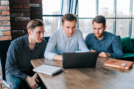 Three young men in an office, discussing work matters while looking at the laptop screen. group of businesspeople in a workplace, having a discussion about new project ideas.の写真素材