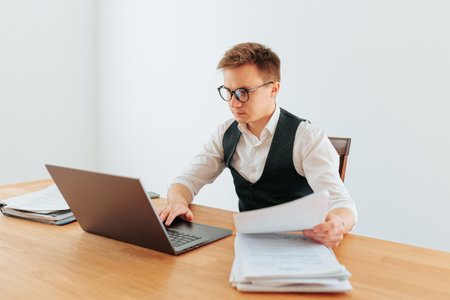 A serious-looking businessman in a white-collar shirt and glasses works from home in his modern office, his laptop open in front of him, as he checks his emails.の写真素材