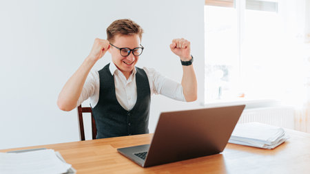 A white collar worker stands alone in his office, hands raised in celebration after a successful product launch. The sense of satisfaction and happiness he feels is evident as he revelの写真素材