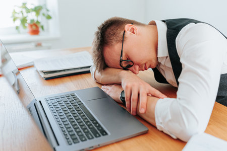 A man with glasses rests his head on his desk, seeking a brief period of slumber to refresh his mind and body before tackling the next project. Rest How Workers are Rediscovering the Benefits Nappingの写真素材