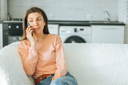 A satisfied young woman enjoying a meal in her cozy kitchen, talking to her sister on her smartphone. The authentic and familiar atmosphere is captured in the photo, with vintage decorationsの写真素材