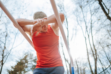 Tired young athlete taking a well-deserved break after mastering the parallel bars. An overworked sportsman feeling drained after an intense parallel bars workout in his red t-shirt.の写真素材