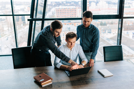 A team of business people collaborating on a project using their laptops. Three young male colleagues working together on laptops in an open office space.の写真素材