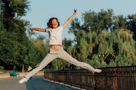 Winner as style of life. Horizontal shot of young beautiful woman in sports clothing smiling while passing finish line during jogging. Evening sunlight on background, Sport lifestyle.の写真素材