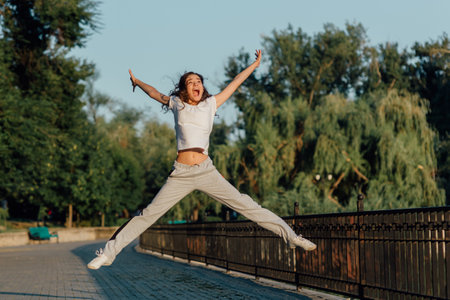 Winner as style of life. Horizontal shot of young beautiful woman in sports clothing smiling while passing finish line during jogging. Evening sunlight on background, Sport lifestyle.の写真素材