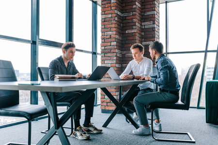 A male mentor leading a group of trainees through a project on their laptops in an indoor work environment. A male mentor providing one-on-one training to a trainee on their laptop in a corporateの写真素材