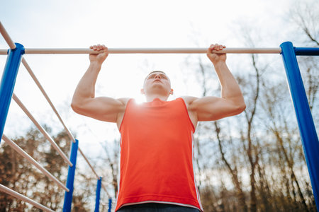 Training for Fitness Competition Active Athlete Doing Pull-Ups at Gym. A young athlete is training for a fitness competition, doing pull-ups on a bar at the gym and pushing himself to be his best.の写真素材